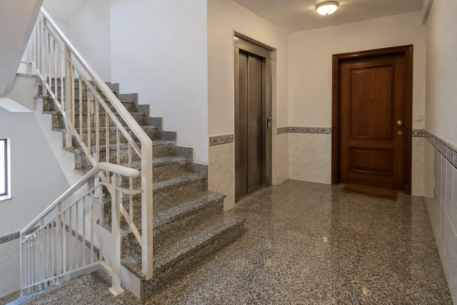 Escadas e patamar de um prédio comum, com degraus em granito e corrimão metálico